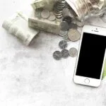 Imagen conceptual con dinero, teléfono y billetera sobre una mesa. Representa control de gastos y herramientas personales para manejar el dinero.