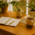 Escritorio con plantas, diario abierto, taza de té y móvil con app de meditación, ejemplificando el manejo emocional.