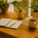 Escritorio con plantas, diario abierto, taza de té y móvil con app de meditación, ejemplificando el manejo emocional.