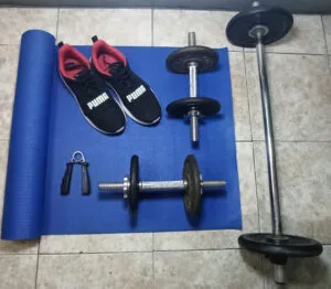 Mi espacio real de entrenamiento en casa: mat, mancuernas, barra y zapatillas, un recordatorio de que los hábitos sostenibles empiezan con lo que ya tenemos.