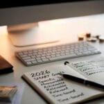 Escritorio con cuaderno abierto mostrando metas financieras SMART para 2026, junto a computadora, dinero y herramientas de planificación.