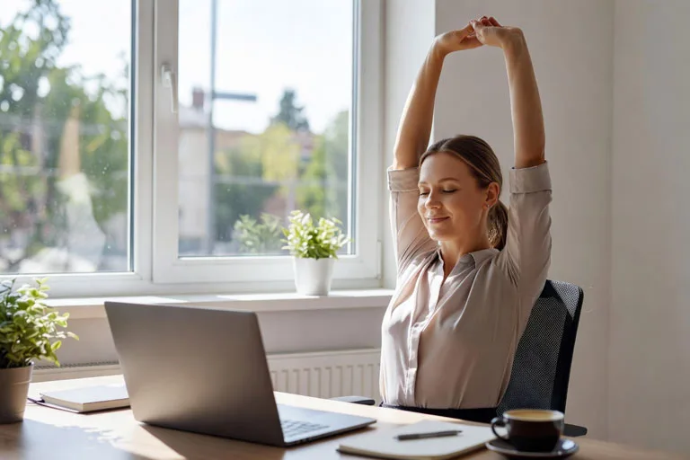 Profesional tomando una pausa activa y estirándose frente al portátil en un espacio de trabajo iluminado, como parte de un hábito saludable para prevenir el agotamiento digital.